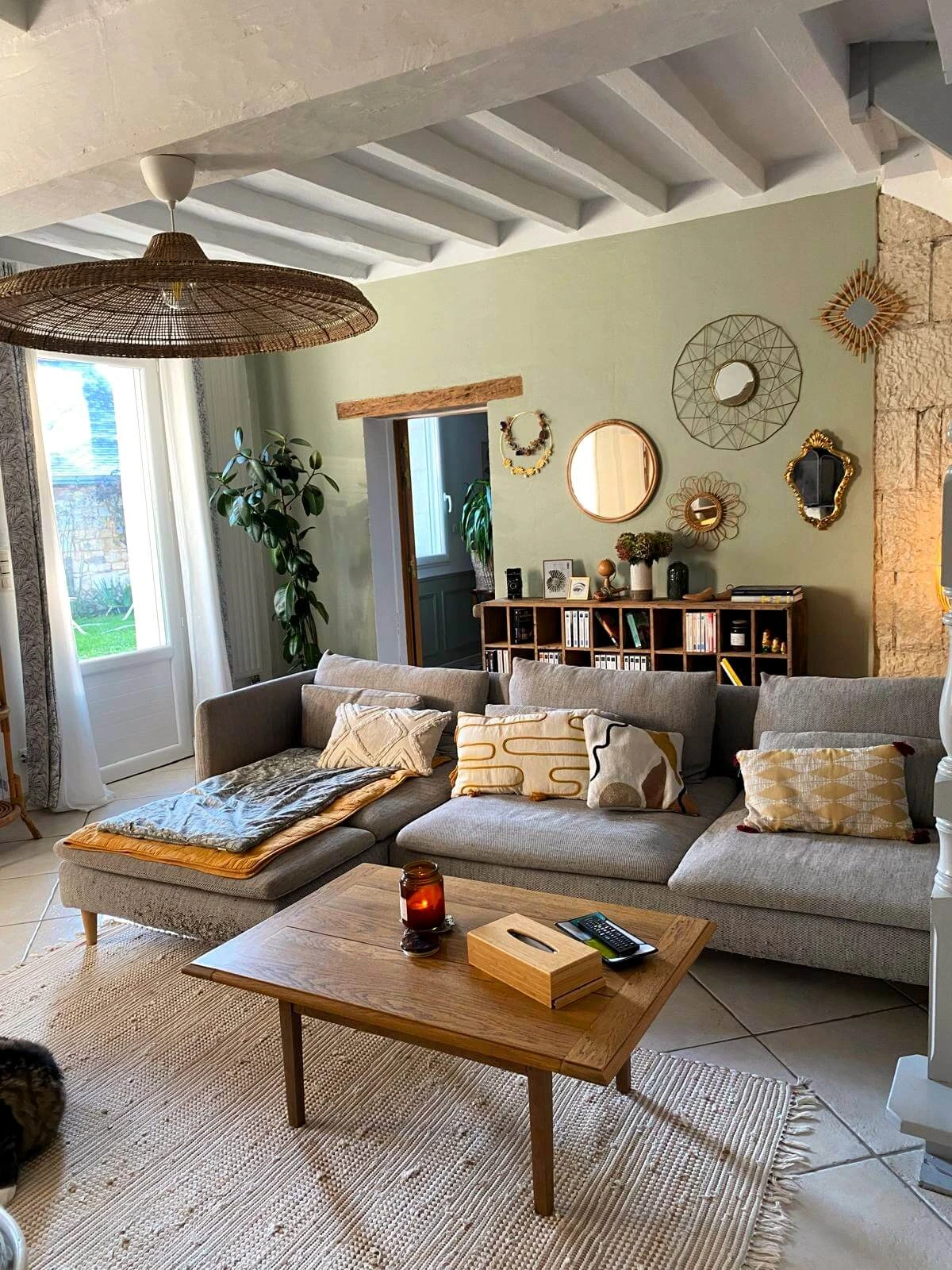 La vue d'ensemble d'un salon ambiance douce et chaleureuse, avec un mur vert de gris et une accumulation de miroirs