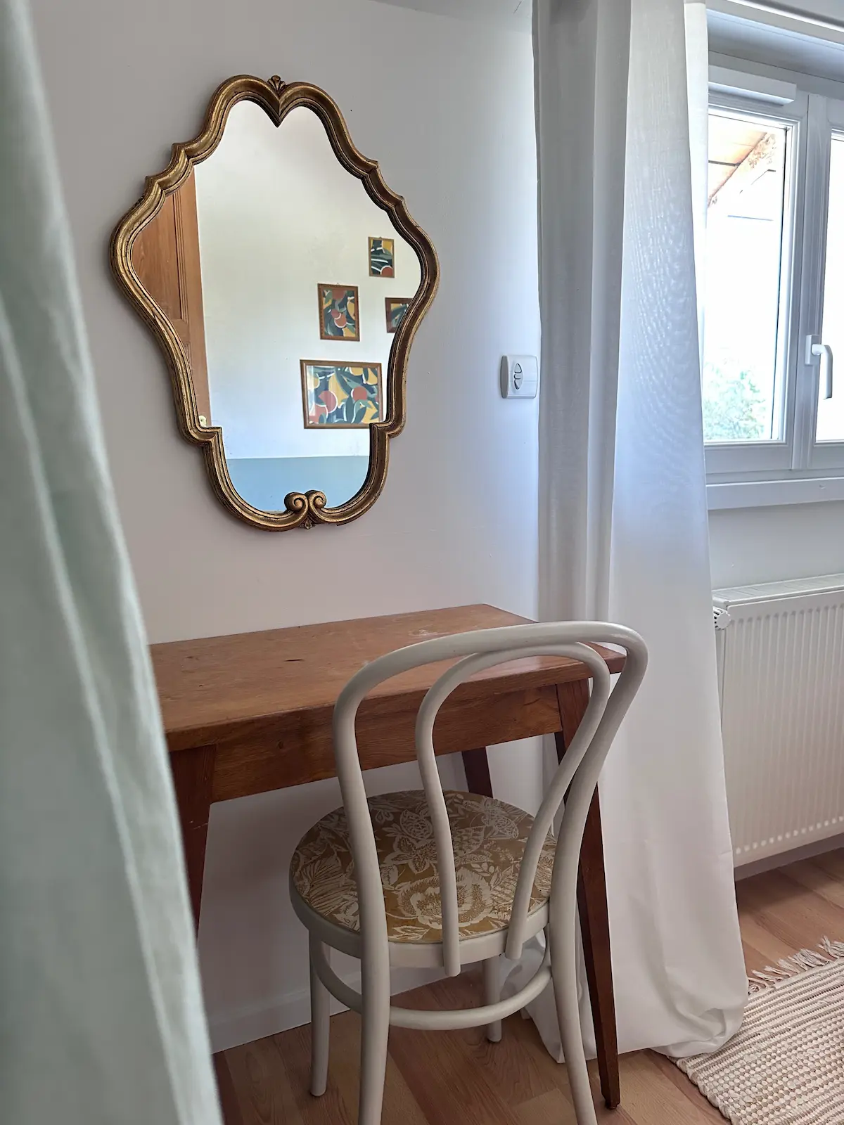 Une petite table ancienne chinée et un miroir doré ancien dans une chambre 